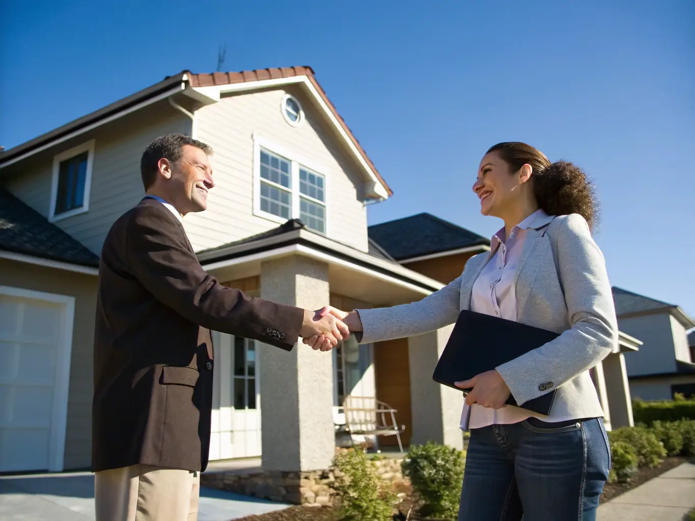A photo of a person shaking hands with a real estate agent in front of a house, symbolizing the initial consultation and agreement.